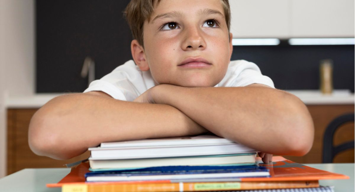 Boy resting his arms on a stack of school books and looking upwards.